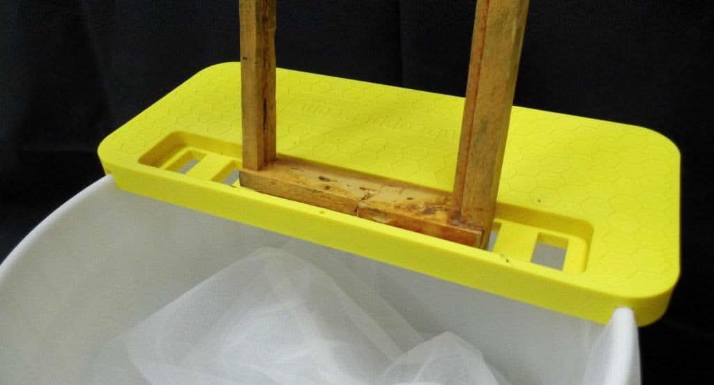 Portable uncapping bench seated across a honey bucket for uncapping frames